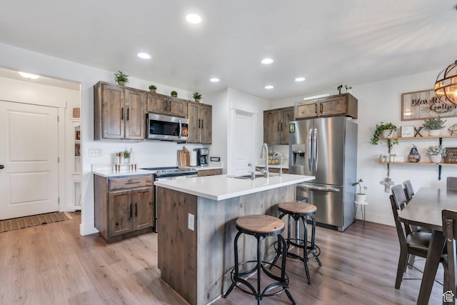 kitchen with appliances with stainless steel finishes, a sink, light wood-type flooring, light countertops, and a kitchen breakfast bar
