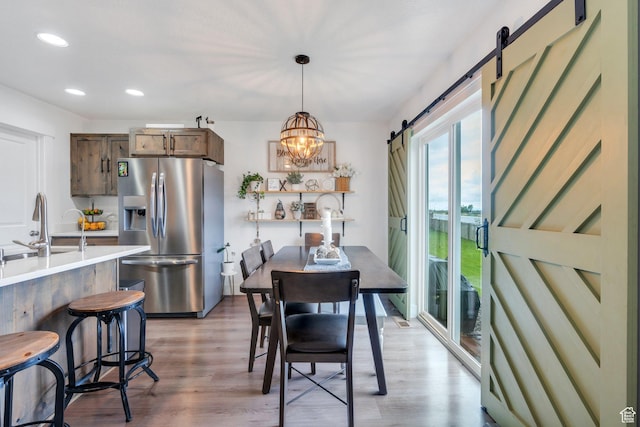 dining space featuring a barn door, light wood-style flooring, recessed lighting, and a chandelier