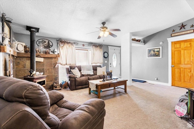 living area featuring a wood stove, a ceiling fan, carpet flooring, a textured ceiling, and baseboards