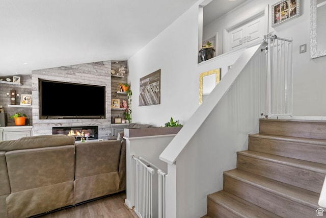staircase featuring vaulted ceiling, wood finished floors, and a glass covered fireplace