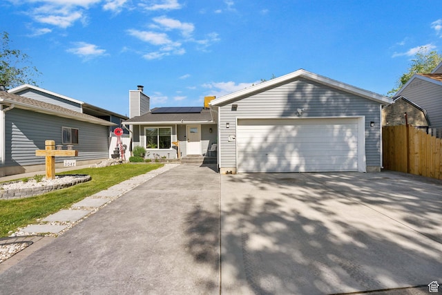 ranch-style home with fence, solar panels, driveway, and an attached garage