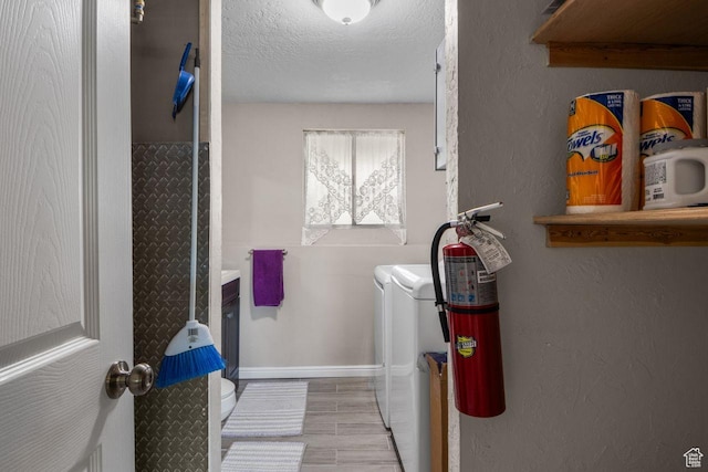 laundry area with washer and dryer, a textured ceiling, baseboards, and a textured wall