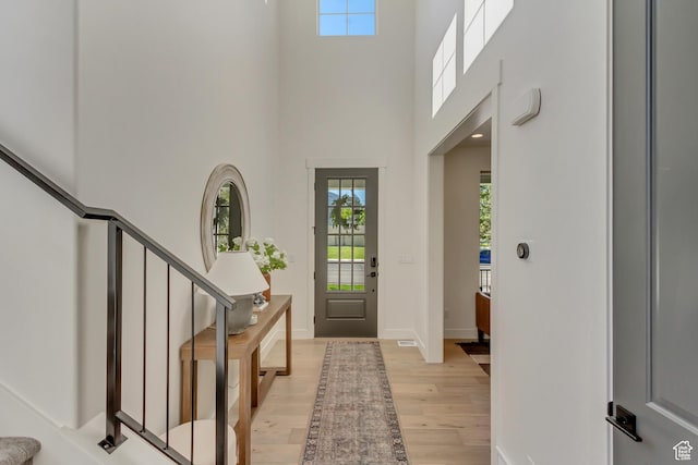 foyer entrance featuring plenty of natural light, light wood-style flooring, a high ceiling, stairway, and baseboards