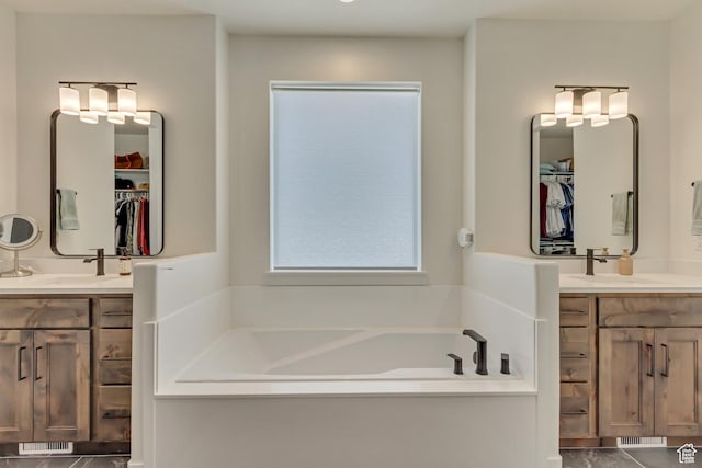 bathroom featuring two vanities, a garden tub, and a walk in closet