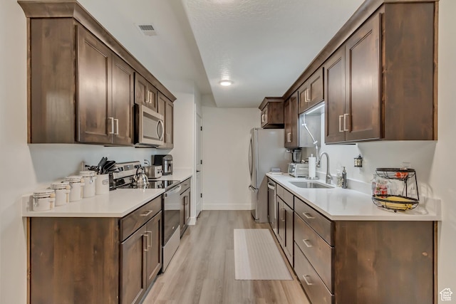 kitchen featuring stainless steel appliances, a sink, light wood-type flooring, dark brown cabinets, and light countertops
