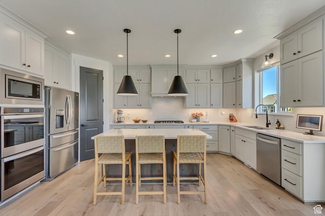 kitchen with stainless steel appliances, a sink, a kitchen island, tasteful backsplash, and light wood-type flooring