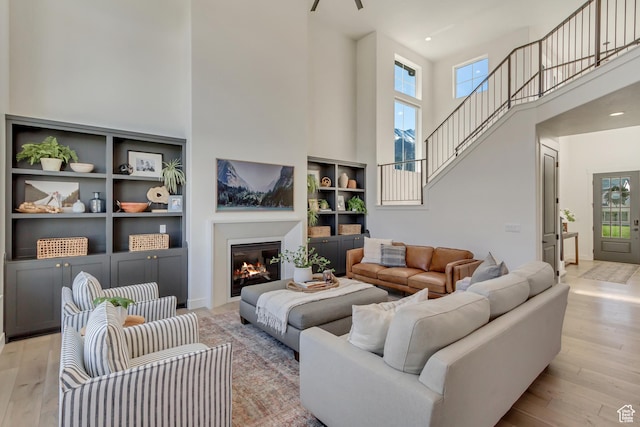 living room with a towering ceiling, plenty of natural light, light wood-style floors, a glass covered fireplace, and built in features