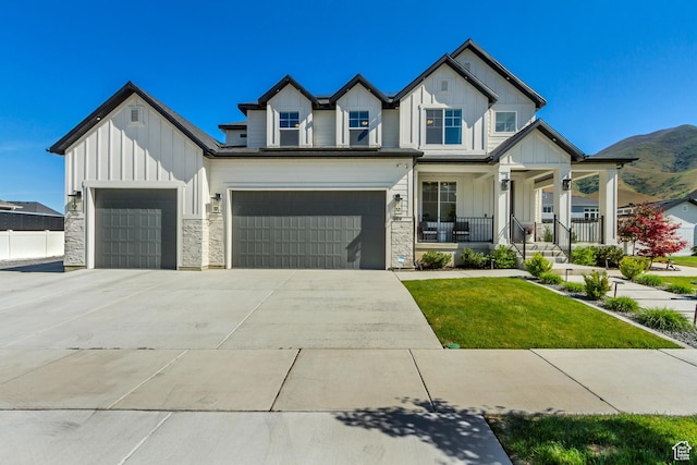 view of front facade featuring board and batten siding, a porch, stone siding, a front yard, and driveway