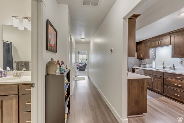 kitchen with a sink, light wood-type flooring, light countertops, and dishwasher