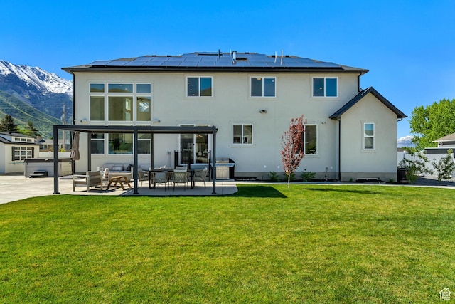 back of house with stucco siding, roof mounted solar panels, a mountain view, and a yard