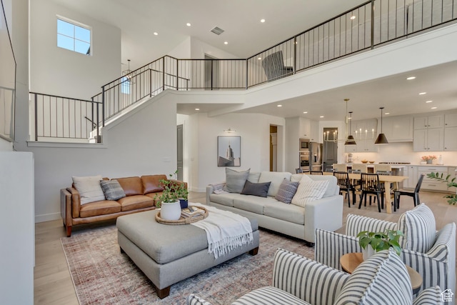 living area with a towering ceiling, light wood-type flooring, recessed lighting, stairway, and baseboards