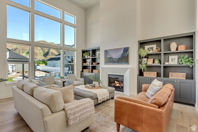 living room featuring a towering ceiling, light wood finished floors, a glass covered fireplace, and baseboards