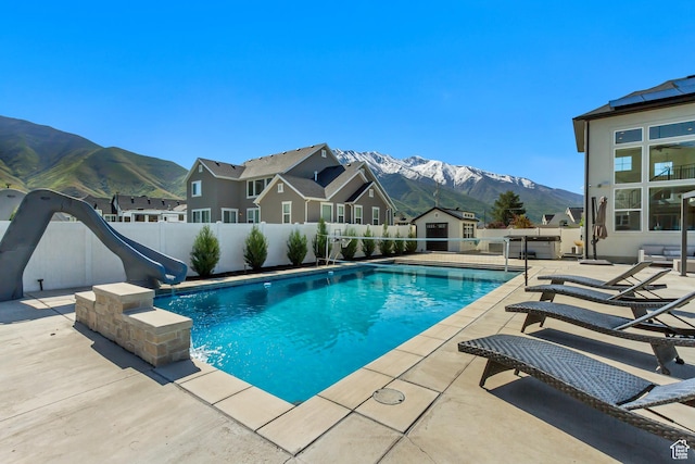 view of pool featuring a water slide, a mountain view, a storage shed, and a patio area