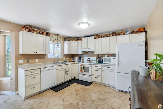kitchen with white appliances, under cabinet range hood, a sink, light tile patterned floors, and a textured ceiling