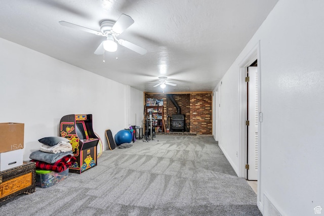 recreation room featuring a wood stove, carpet floors, a ceiling fan, and a textured ceiling