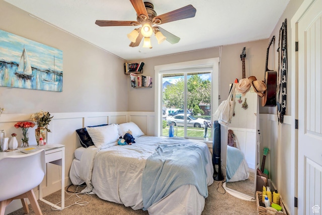 carpeted bedroom featuring a wainscoted wall and a ceiling fan