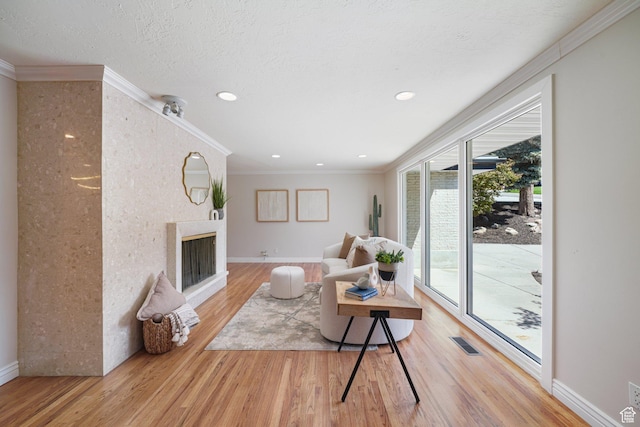 living room featuring wood finished floors, a fireplace, crown molding, baseboards, and recessed lighting