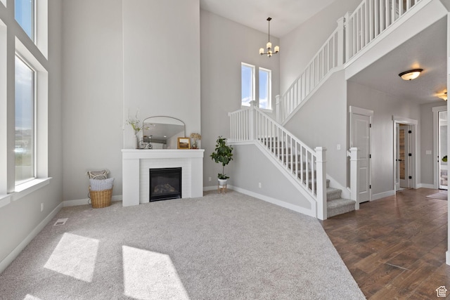 living room featuring a towering ceiling, stairway, a glass covered fireplace, a chandelier, and baseboards