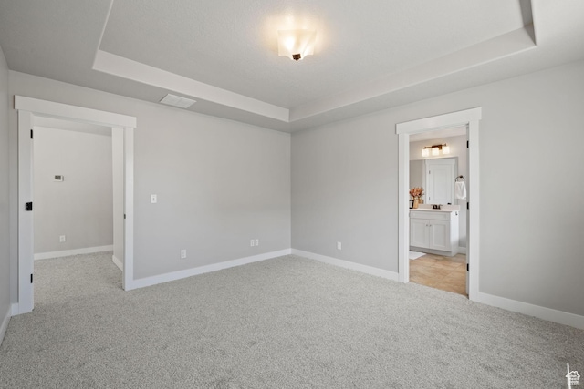 unfurnished room featuring a tray ceiling, light carpet, and baseboards