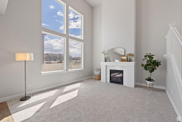unfurnished living room with carpet flooring, healthy amount of natural light, a glass covered fireplace, baseboards, and a high ceiling