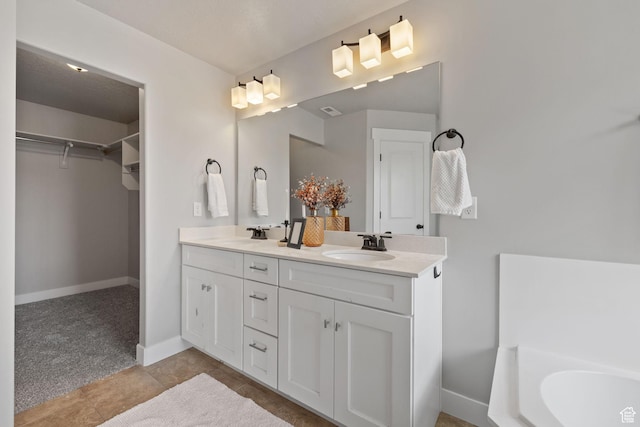 bathroom with a spacious closet, double vanity, baseboards, and a bath