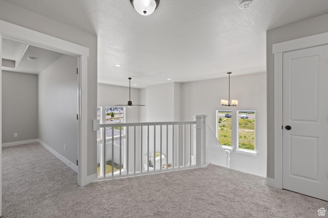 hall with carpet, a chandelier, baseboards, and an upstairs landing