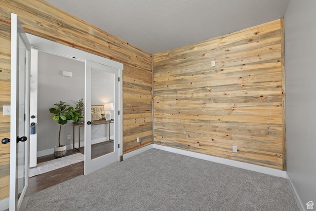 unfurnished room with wood walls, french doors, carpet, and baseboards