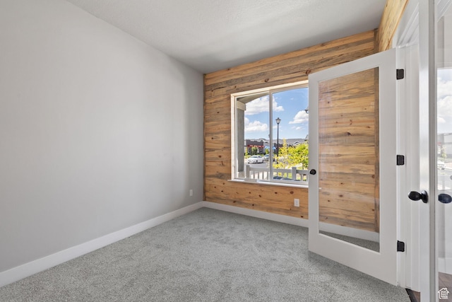 carpeted empty room featuring wood walls and baseboards