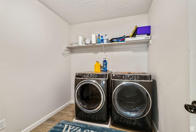 washroom featuring washing machine and dryer, wood finished floors, a textured ceiling, and baseboards