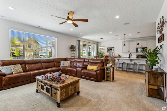 living area with ceiling fan, a textured ceiling, light carpet, and recessed lighting