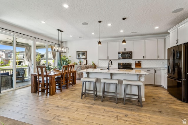 kitchen with black appliances, a sink, decorative backsplash, light stone countertops, and a textured ceiling