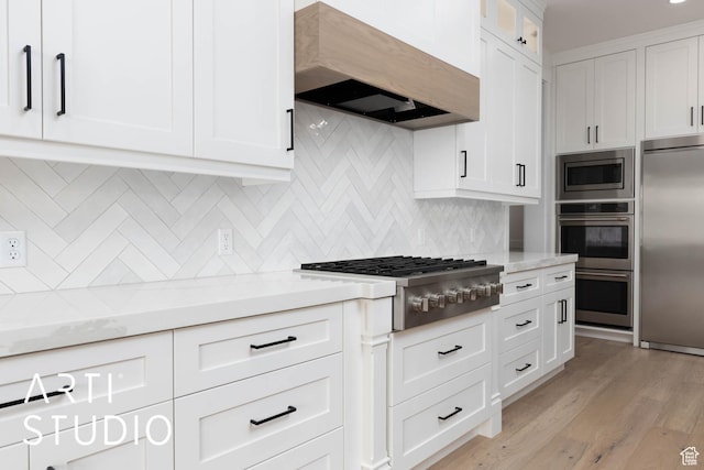kitchen featuring built in appliances, range hood, white cabinetry, and light stone countertops