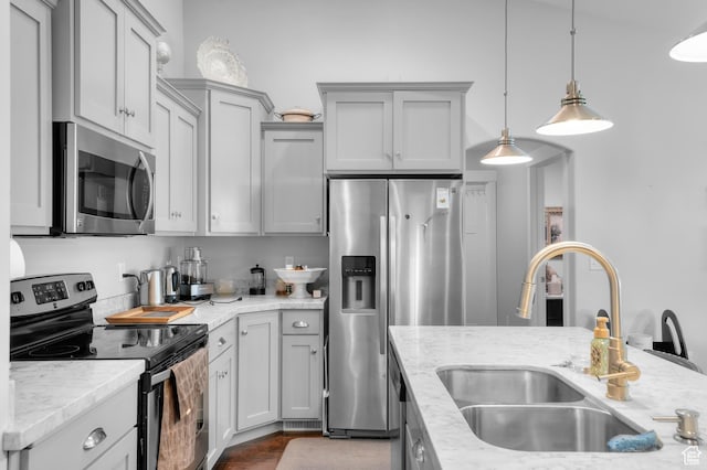 kitchen with appliances with stainless steel finishes, a sink, decorative light fixtures, light stone countertops, and gray cabinets