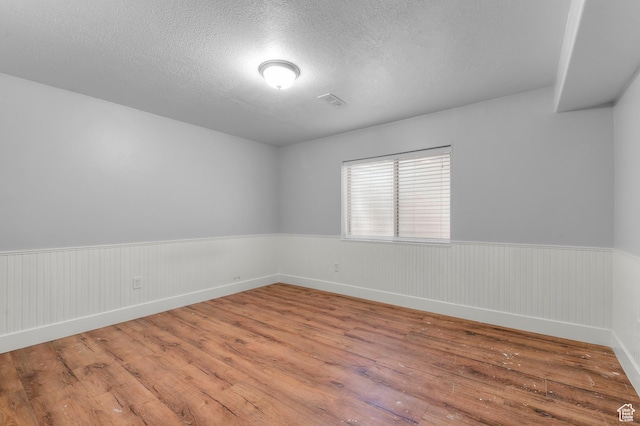 empty room with hardwood / wood-style floors, wainscoting, and a textured ceiling