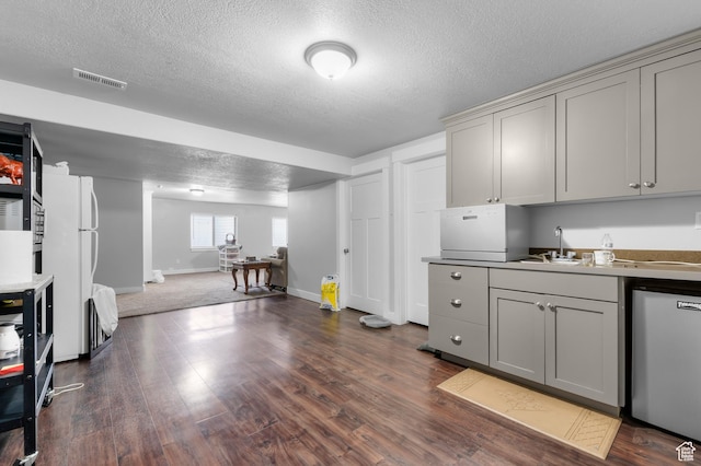 kitchen with gray cabinets, dishwashing machine, a textured ceiling, and dark wood-type flooring
