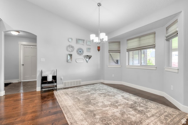 unfurnished dining area with dark wood finished floors, baseboards, and arched walkways