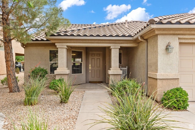 entrance to property featuring a tiled roof, an attached garage, and stucco siding