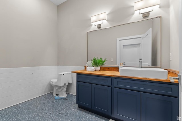 bathroom featuring a wainscoted wall, toilet, vanity, and tile walls