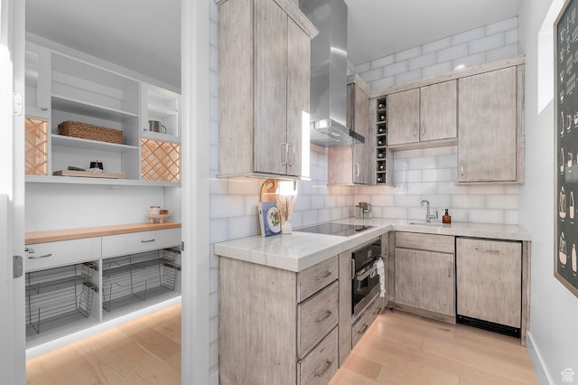 kitchen with oven, light wood-style flooring, wall chimney exhaust hood, light countertops, and backsplash