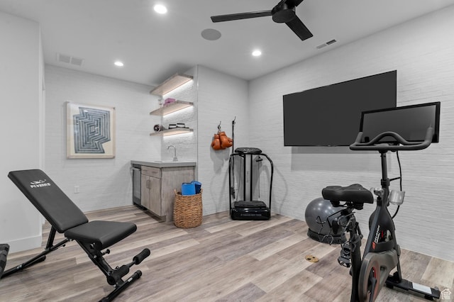 exercise area with ceiling fan, light wood-type flooring, recessed lighting, brick wall, and bar area