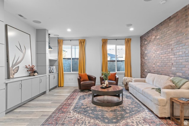 living area with brick wall, light wood-style flooring, plenty of natural light, recessed lighting, and an accent wall