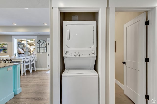 clothes washing area with stacked washer / drying machine, baseboards, light wood finished floors, and recessed lighting