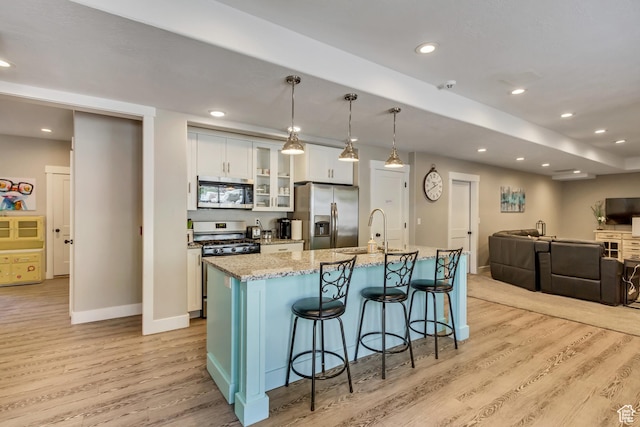 kitchen featuring stainless steel appliances, light wood finished floors, white cabinetry, an island with sink, and recessed lighting