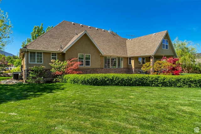 rear view of property featuring central AC, a lawn, stucco siding, and roof with shingles