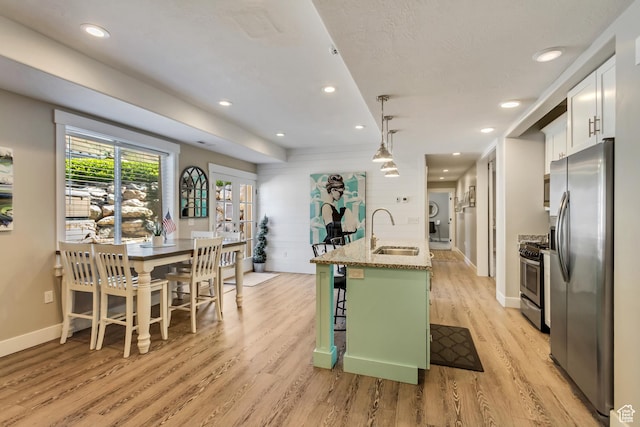 kitchen featuring appliances with stainless steel finishes, a sink, light wood finished floors, white cabinetry, and a breakfast bar