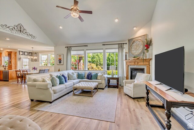 living room featuring high vaulted ceiling, a ceiling fan, a glass covered fireplace, light wood-type flooring, and a chandelier