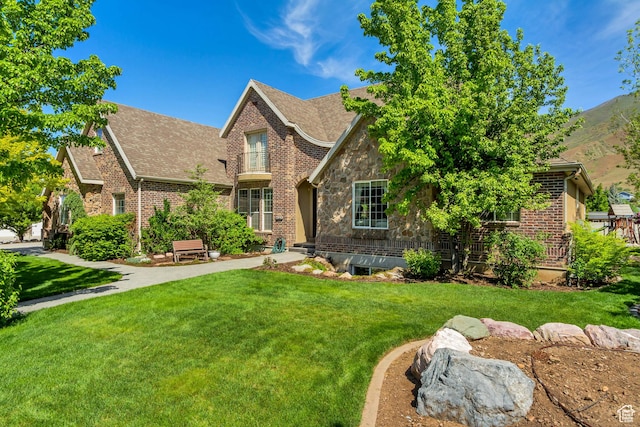 tudor house featuring a front lawn, a shingled roof, stone siding, and brick siding