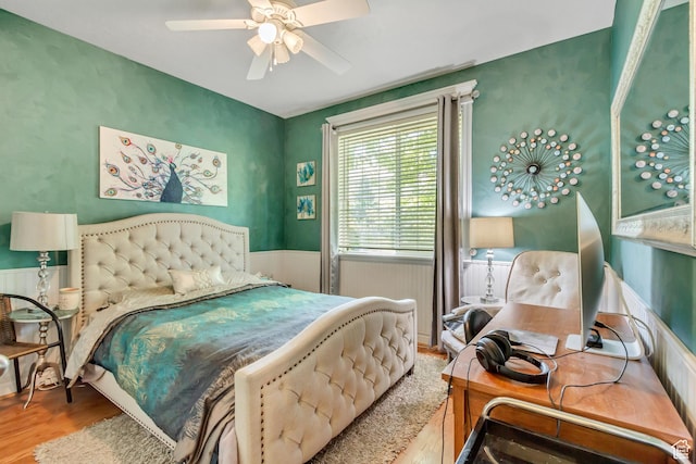 bedroom featuring wood finished floors, wainscoting, and a ceiling fan