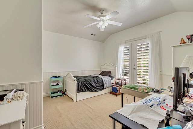 carpeted bedroom featuring vaulted ceiling, wainscoting, and a ceiling fan