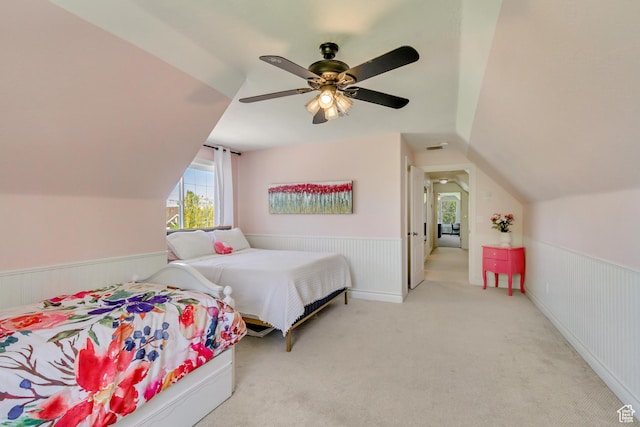 bedroom featuring multiple windows, lofted ceiling, wainscoting, carpet, and a ceiling fan